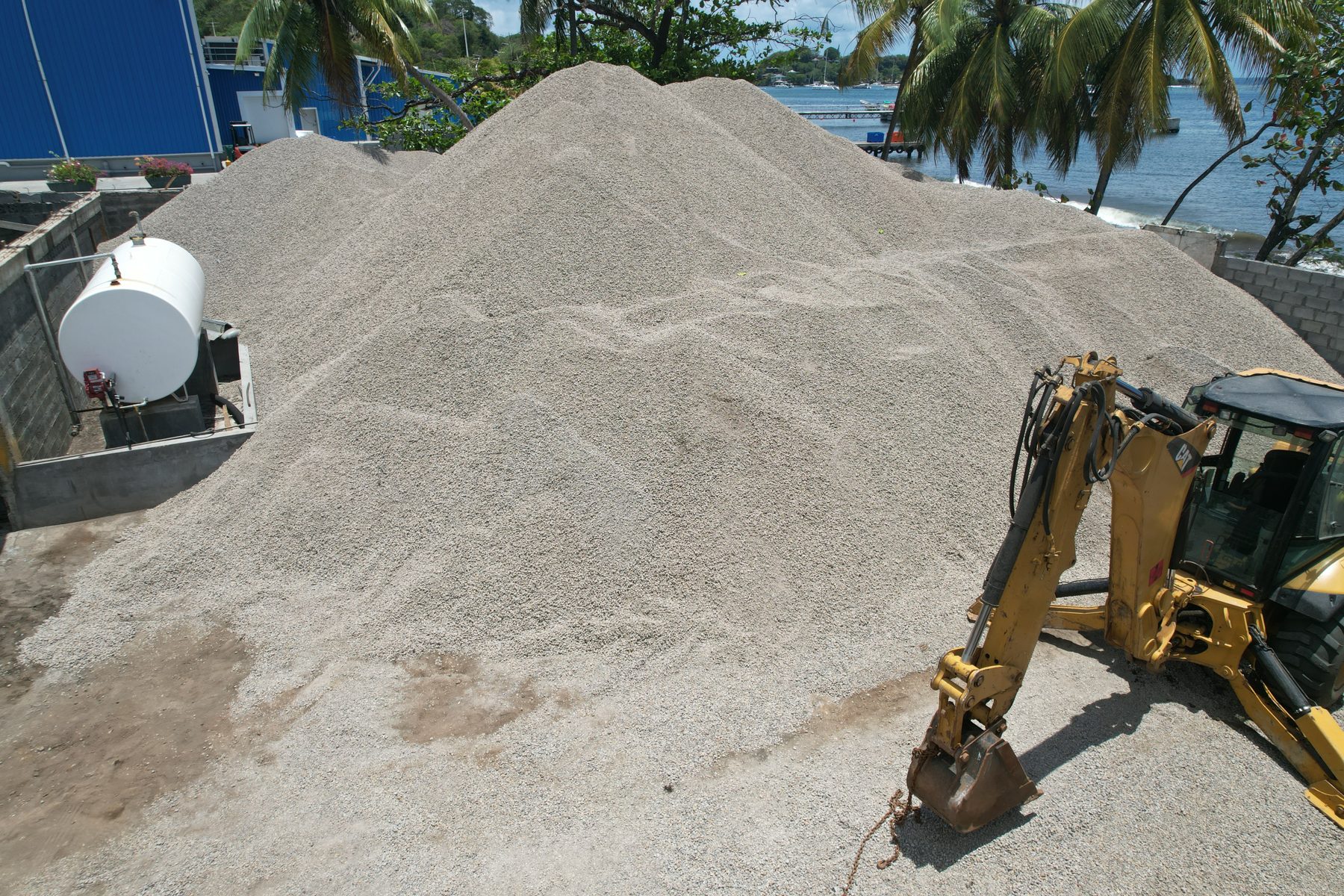 Backhoe at aggregate pile beside the sea